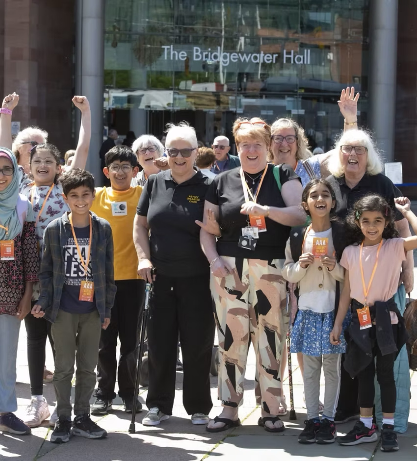 Children and older people from an Intergenerational Music Making group cheering outside The Bridgewater Hall in Manchester