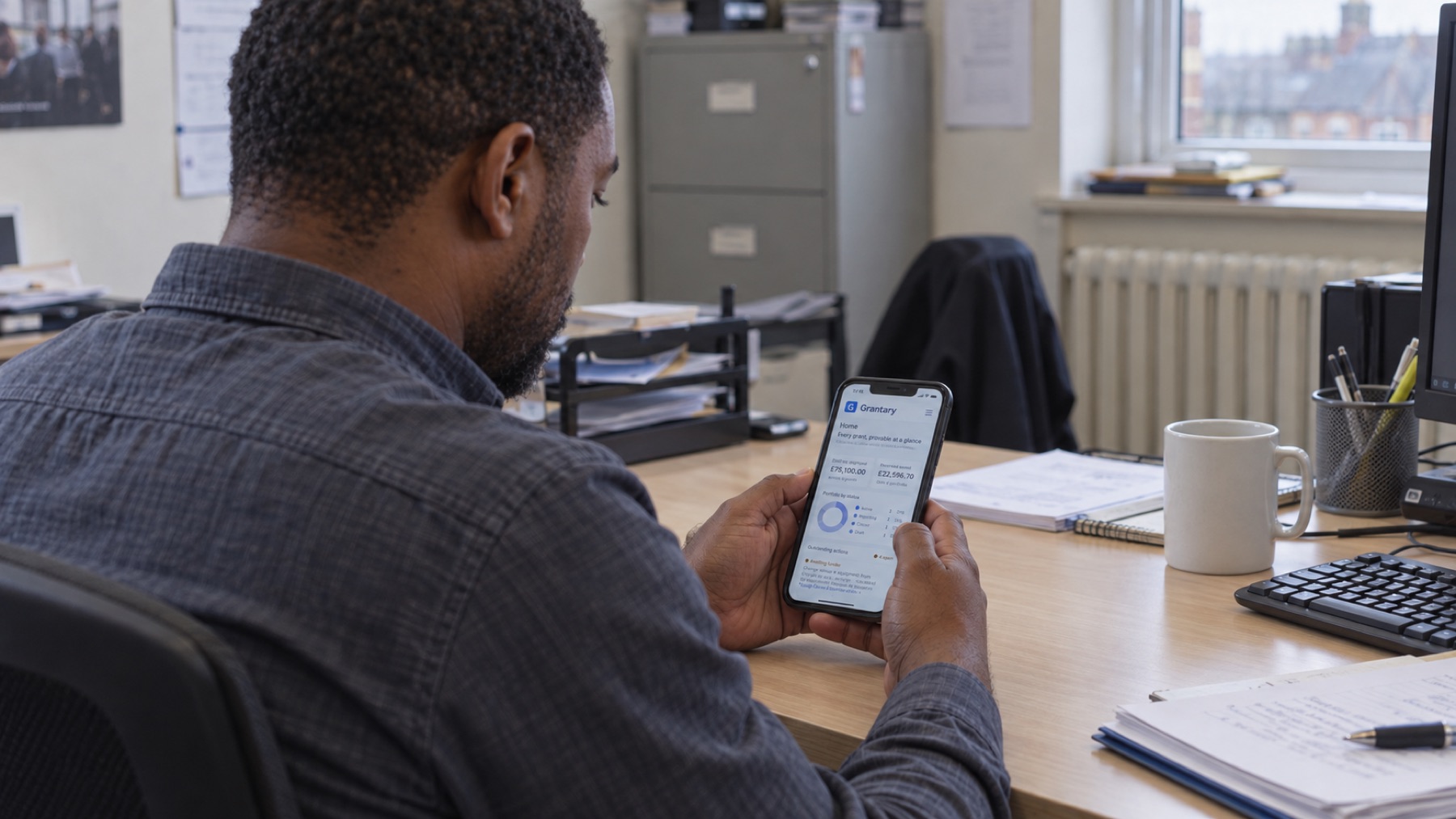 A charity worker at a desk reading the Grantary home screen on his phone